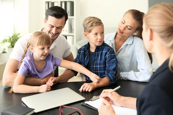 Familie sitzt einer Frau an einem Tisch gegenüber